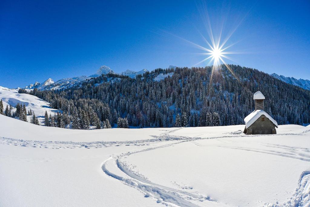 a sun shines over a snow covered mountain with a church at Hotel Beauregard in La Clusaz