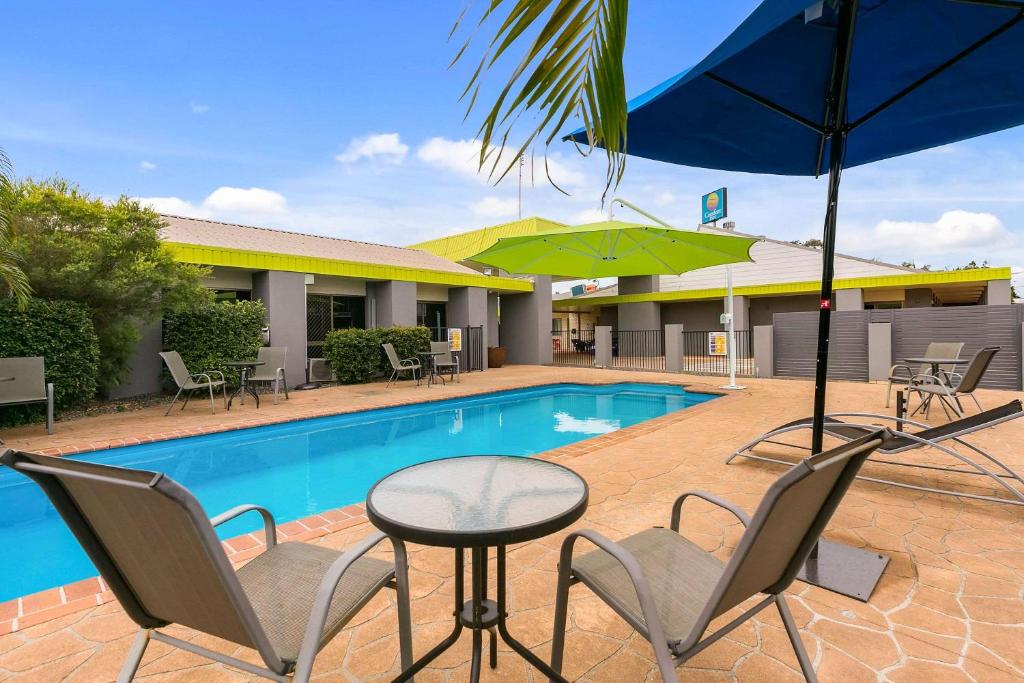 - une piscine avec des chaises, une table et un parasol dans l'établissement Comfort Inn on Main Hervey Bay, à Hervey Bay