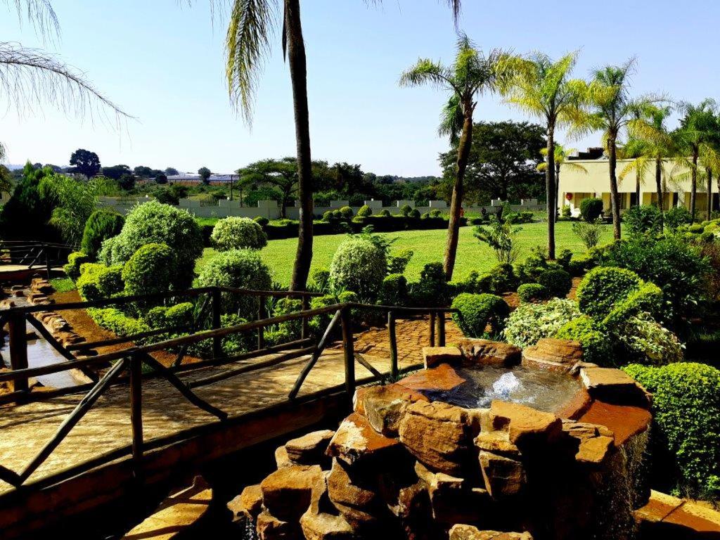 a garden with a fountain and palm trees and bushes at Naledzi Hotel & Conference centre in Thohoyandou