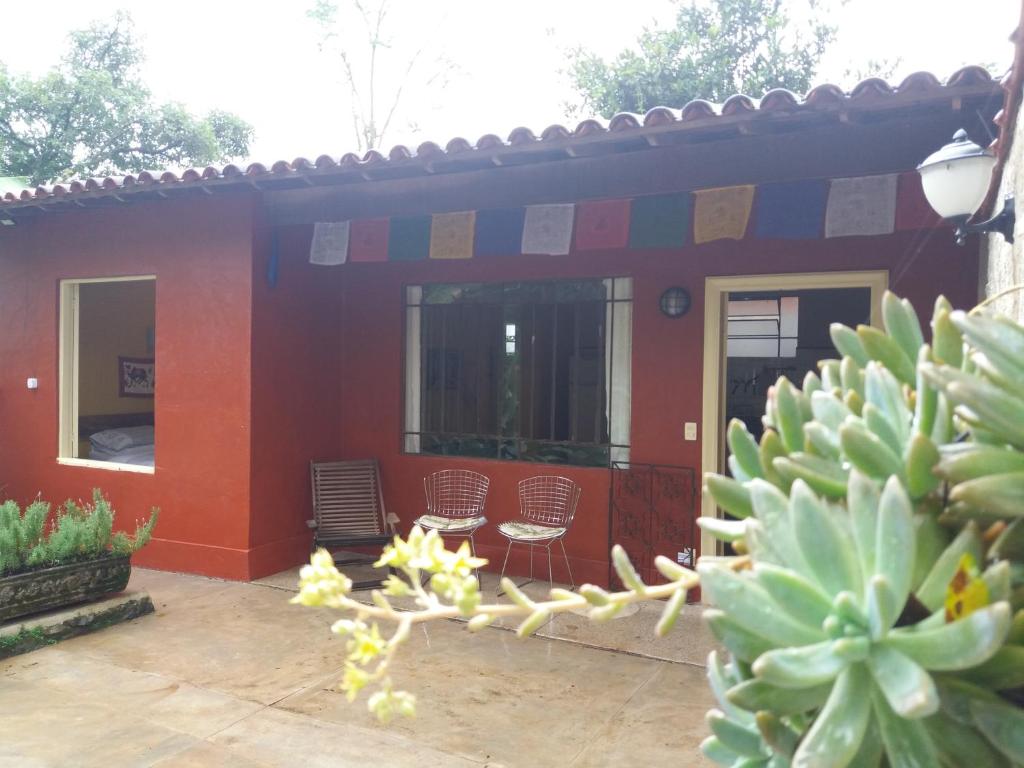une maison rouge avec des chaises et un cactus dans l'établissement "Chalé Balines Oroboro" 1 - Casa com jardim de 150 m e cozinha completa em Macacos, à Macacos