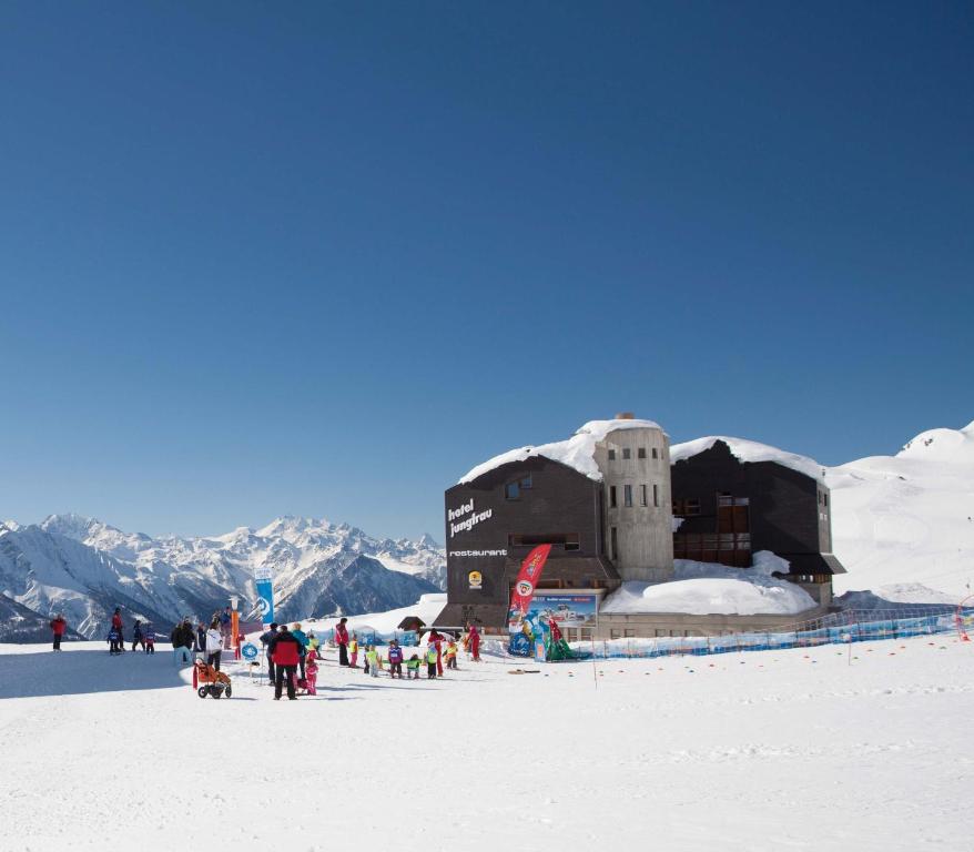 un grupo de personas de pie alrededor de un edificio en la nieve en Hotel Jungfrau en Fiesch