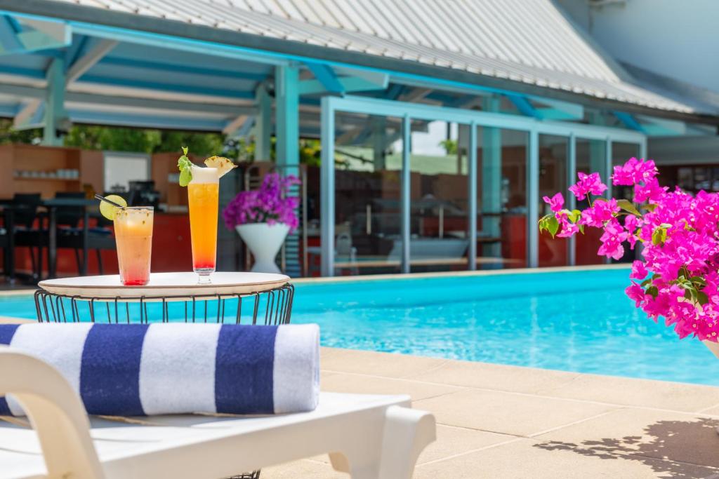 Zwei Cocktails stehen auf einem Tisch neben einem Pool. in der Unterkunft The Originals City, Hôtel Belova, Cayenne Sud in Montjoly