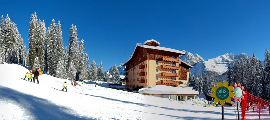 un grupo de personas esquiando por una pista cubierta de nieve junto a un edificio en Carlo Magno Hotel Spa Resort, en Madonna di Campiglio