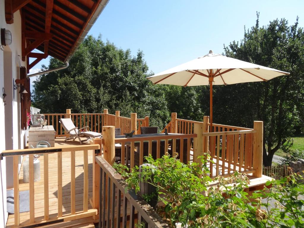 una terraza de madera con sombrilla y silla en Maison d'hôtes l'Arnica en La Bréole