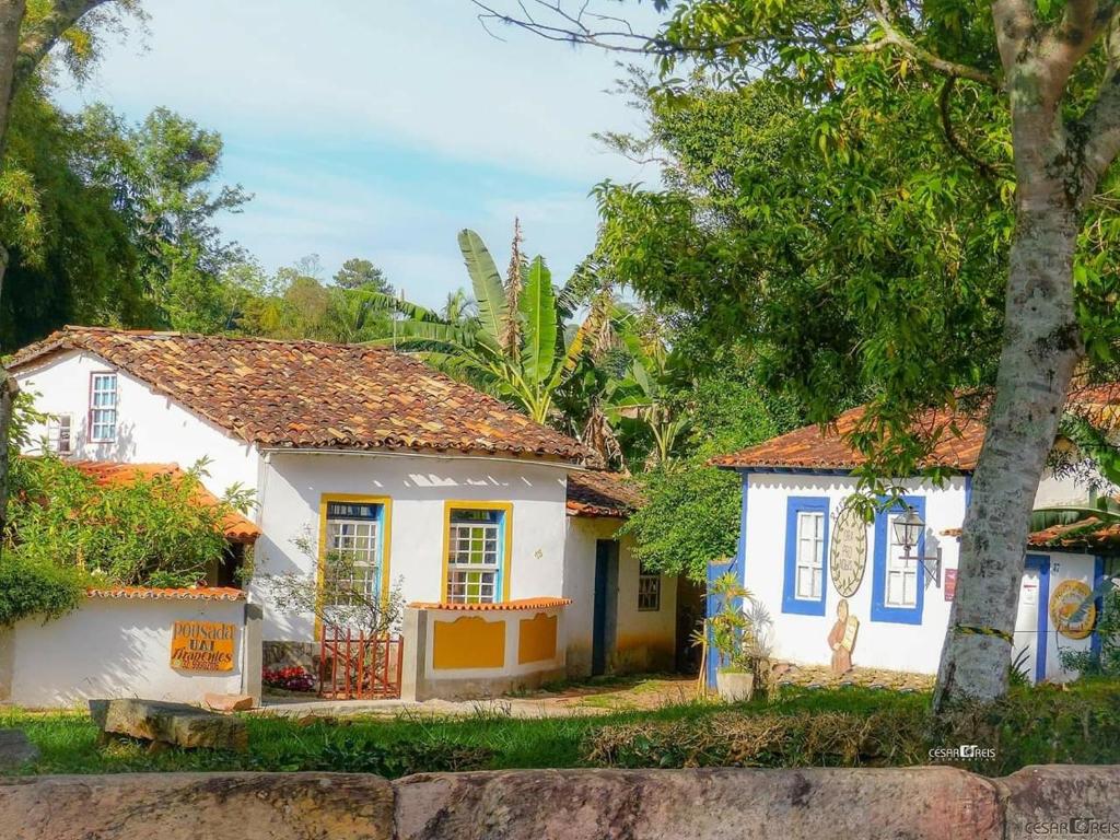 a small white house with blue windows and trees at Pousada Uai Tiradentes in Tiradentes
