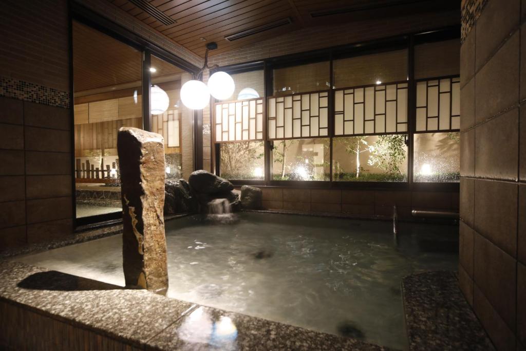 a bath tub with a stone pillar in a room with windows at Dormy Inn Premium Osaka Kitahama in Osaka