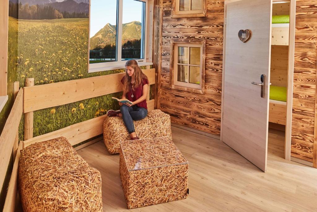 a woman sitting on a bench reading a book in a cabin at Arena Hostel Allgäu in Sonthofen
