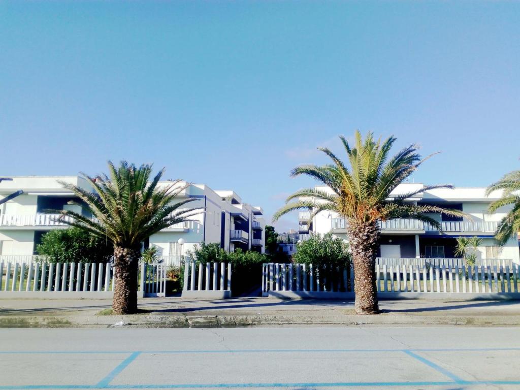 two palm trees in front of a white fence at Residenze Sul Mare in Martinsicuro