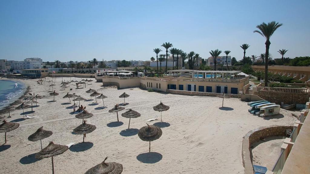 a beach with umbrellas on the sand near the water at Hotel Les Palmiers in Monastir