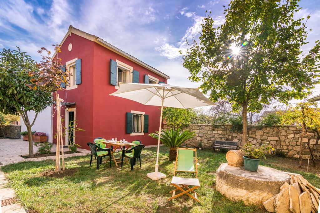 a red house with a table and chairs and an umbrella at Traditional Rustic Maisonette by Konnect in Agios Ioannis Peristeron
