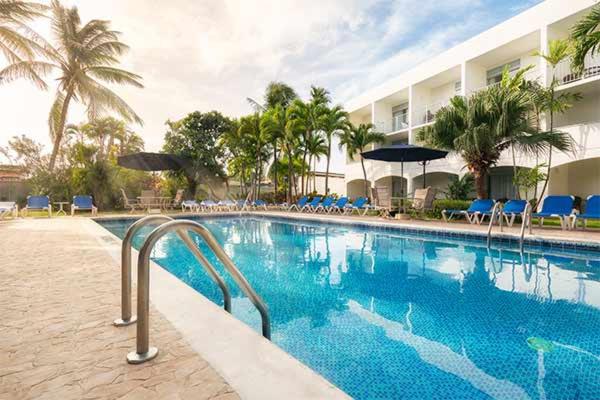 a swimming pool with chairs and umbrellas next to a hotel at Time Out Hotel in Christ Church