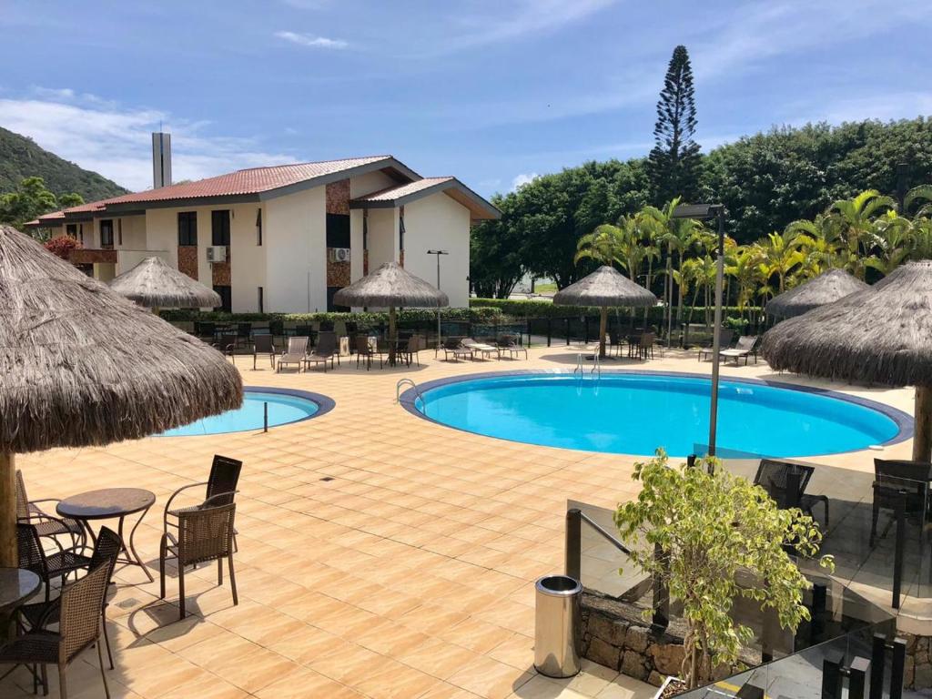 una piscina con sillas, mesas y sombrillas en AP em Floripa 2 quartos a 100m da praia - PRAIA BRAVA- NORTE DA ILHA, en Florianópolis