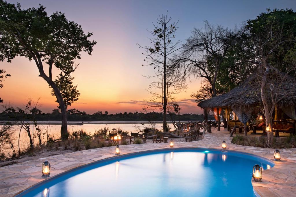 a resort pool with a sunset in the background at Selous River Camp in Kwangwazi