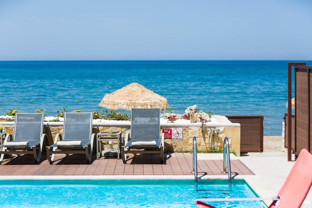a pool with chairs and an umbrella and the ocean at Espera, Luxury Beach Front Residence, By ThinkVilla in Rethymno