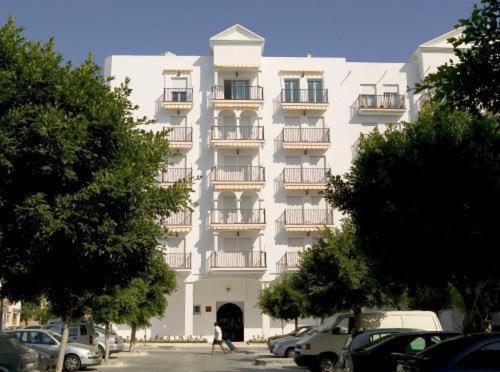 un gran edificio blanco con balcones y coches estacionados frente a él en Apartamentos Miguel Angel, en Estepona