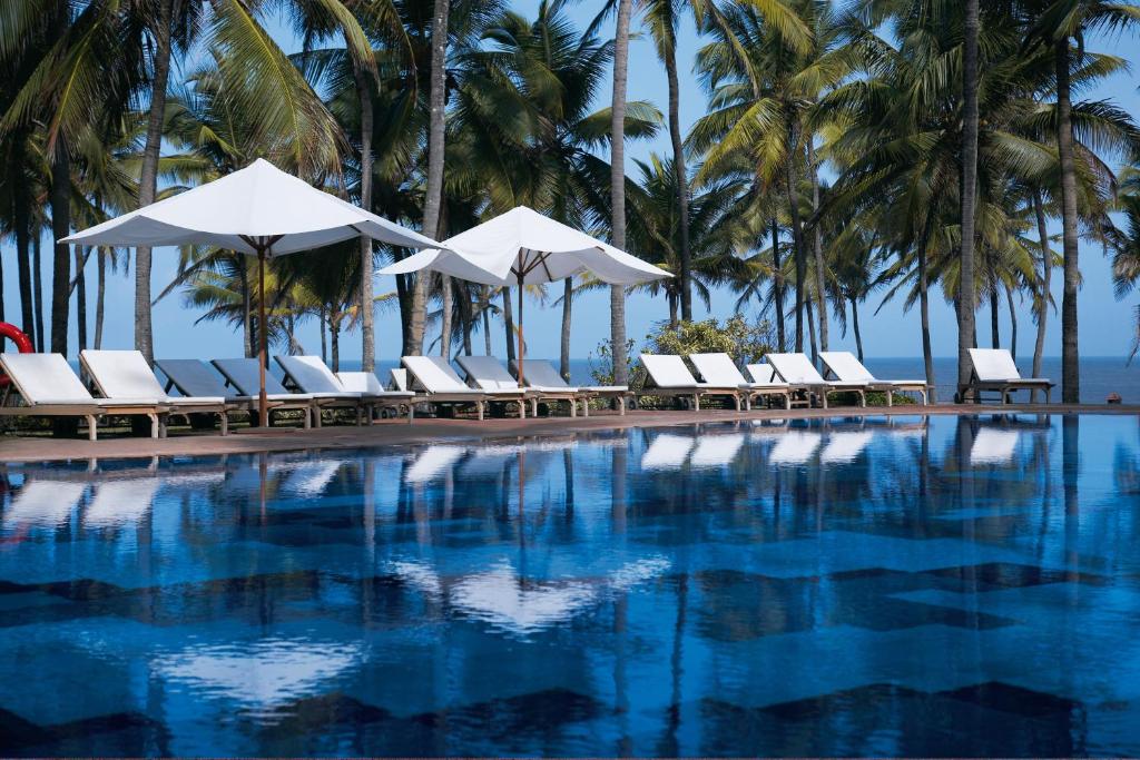 a pool with chairs and umbrellas and palm trees at Taj Holiday Village Resort & Spa, Goa in Candolim