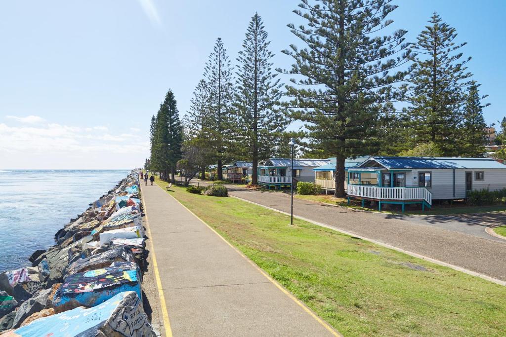 einen Bürgersteig neben einem Wasserkörper mit Häusern in der Unterkunft NRMA Port Macquarie Breakwall Holiday Park in Port Macquarie