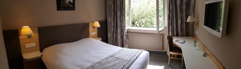 a bedroom with a bed and a desk and a window at Hotel Les Remparts in Kaysersberg