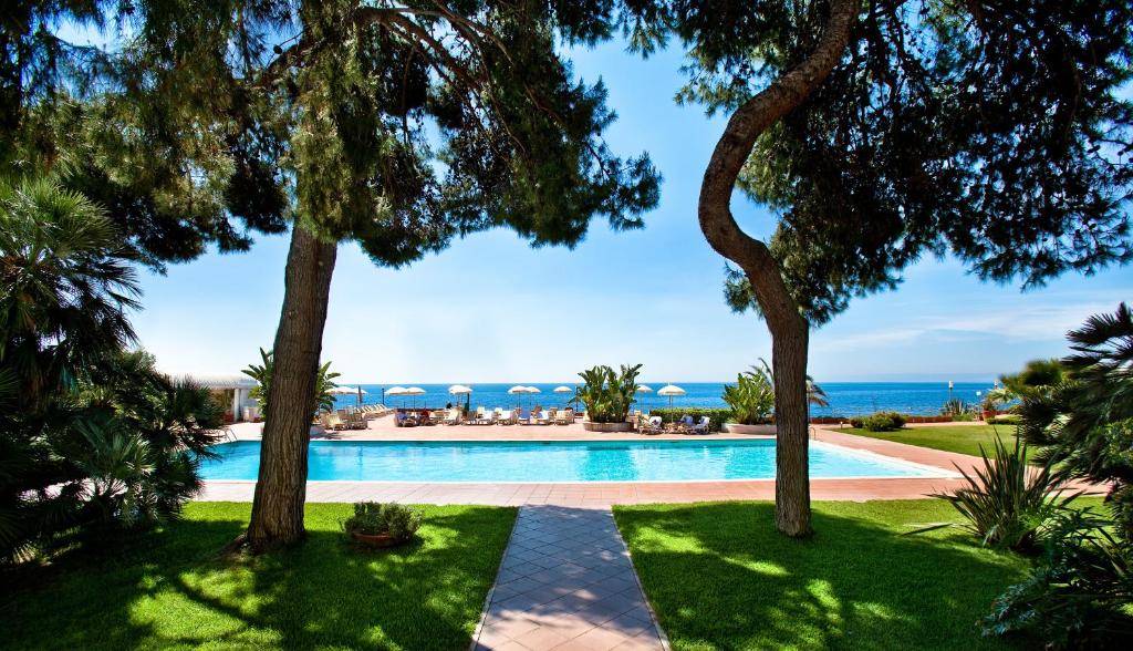 een zwembad met bomen en de oceaan op de achtergrond bij Grand Hotel Baia Verde in Catania