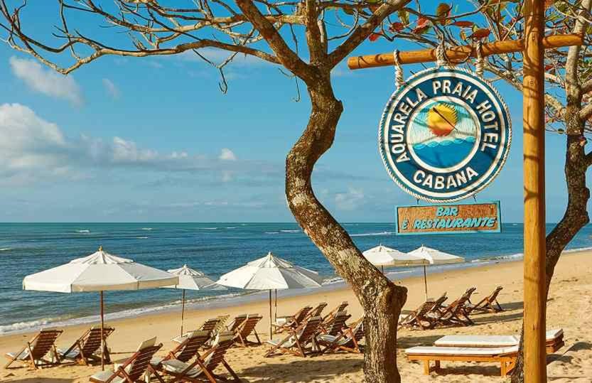 uma placa numa praia com cadeiras e guarda-sóis em Aquarela Praia Hotel em Arraial d'Ajuda