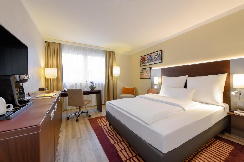 a bedroom with a large white bed and a desk at Mercure Hotel Duisburg City in Duisburg