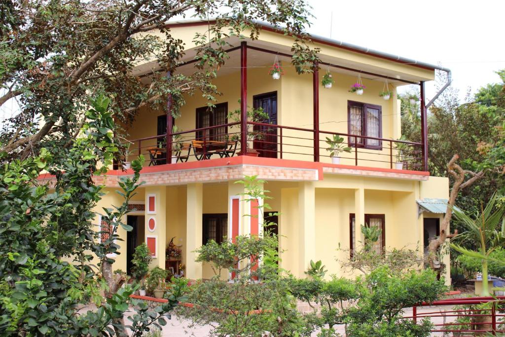 Nguyet Que Homestay & Tours في Ben Tre: منزل أصفر مع شرفة فوقه