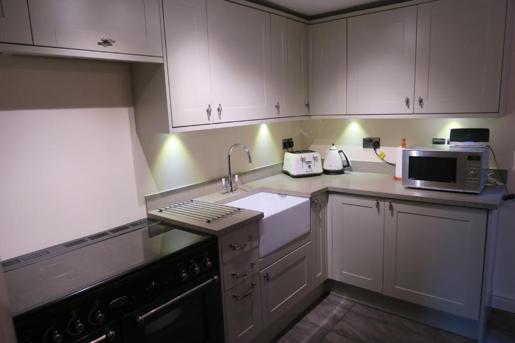 a kitchen with white cabinets and a sink and a microwave at Coniston Cottage Lake View in Coniston