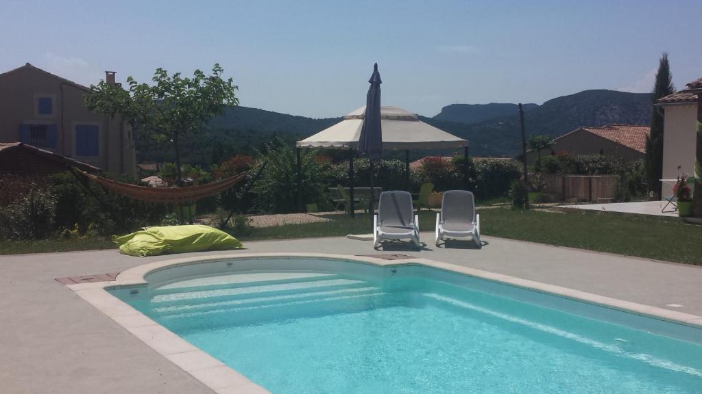 uma piscina com duas cadeiras e um guarda-sol em Le petit Ventoux em Malaucène