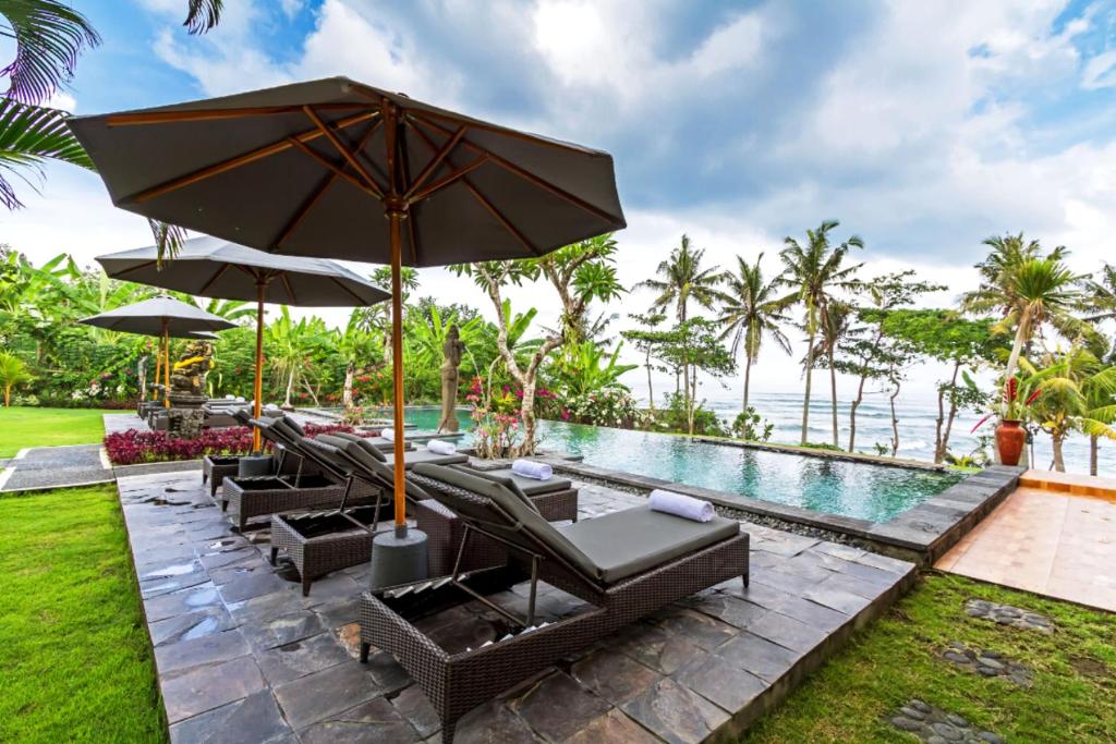 een terras met stoelen en een parasol en een zwembad bij Bali Natha Beach Front in Canggu