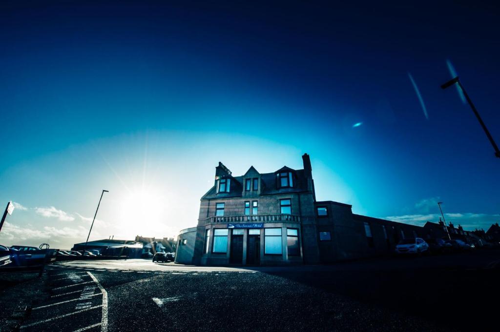 a building in a parking lot with the sun behind it at Seaview Hotel in Peterhead
