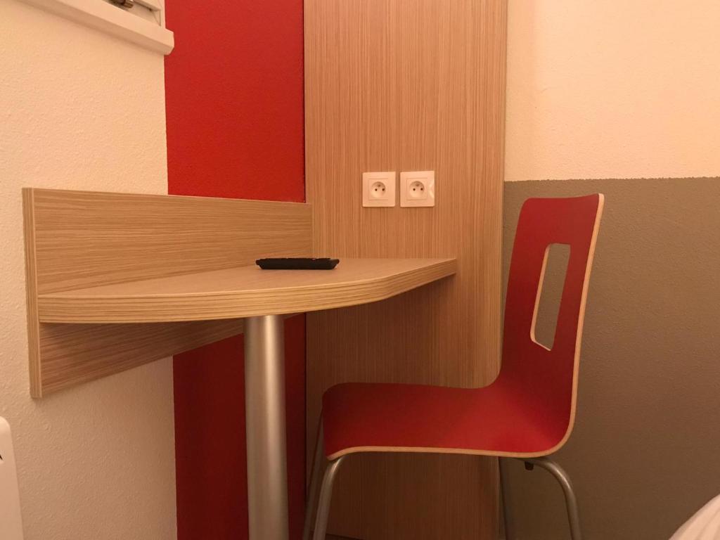 a red chair sitting next to a table in a room at Première Classe Reims Ouest - Tinqueux in Reims