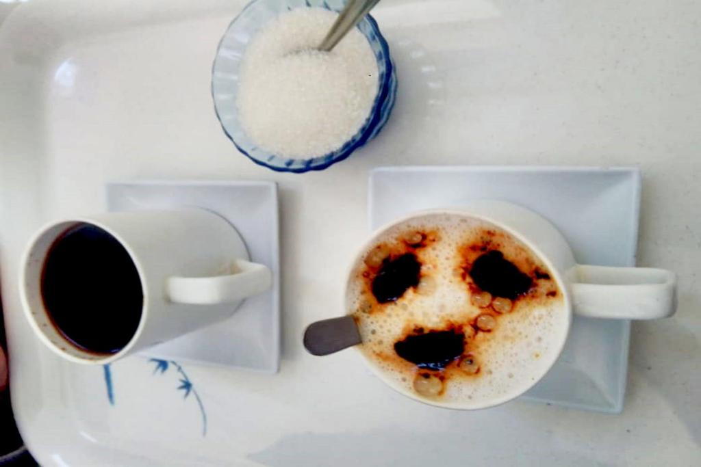 a table with a cup of coffee and a bowl of sugar at Landy Queen in Munnar
