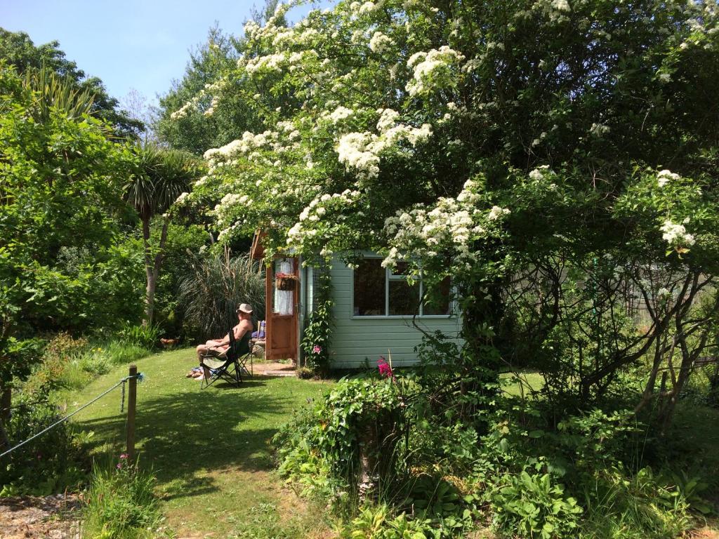 a man sitting in a chair in front of a green house at Millbrook in Helston