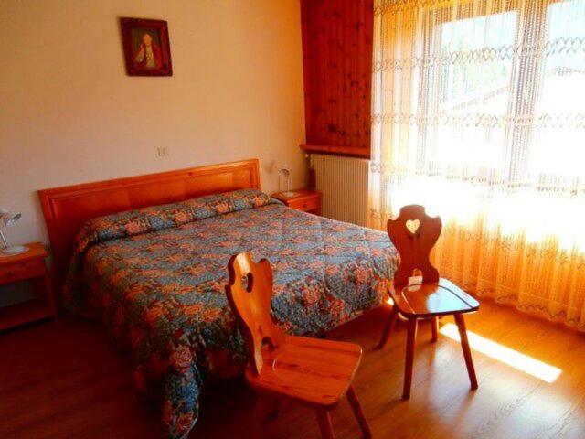 a bedroom with a bed and two wooden chairs at Appartamento lerpino in Sappada