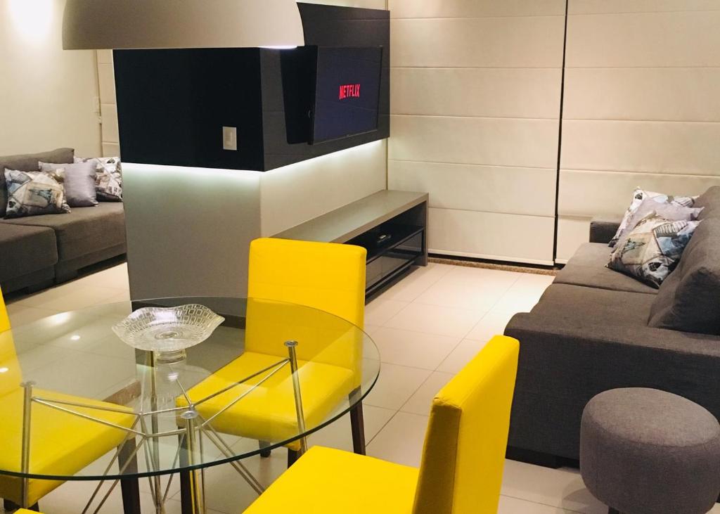 - un salon avec une table en verre et des chaises jaunes dans l'établissement Apartamento na Ponta Verde Maceió Facilities, à Maceió