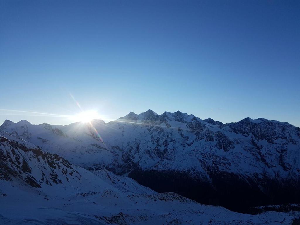 a sun setting over a snow covered mountain range at Sunshine in Saas-Grund
