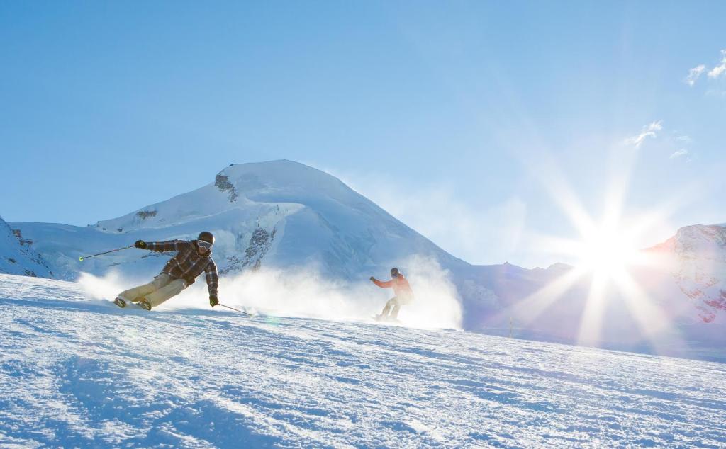 two people are skiing down a snow covered slope at Sunshine in Saas-Grund