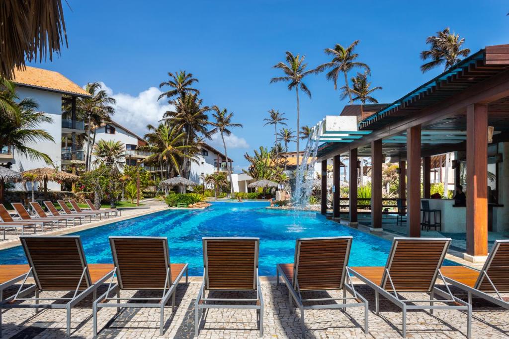 een zwembad in het resort met stoelen en palmbomen bij Apartamento no Taiba Beach Resort in Taíba