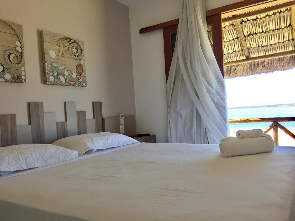1 dormitorio con 1 cama blanca grande y ventana en Pousada Portal da Ilha en Itarema