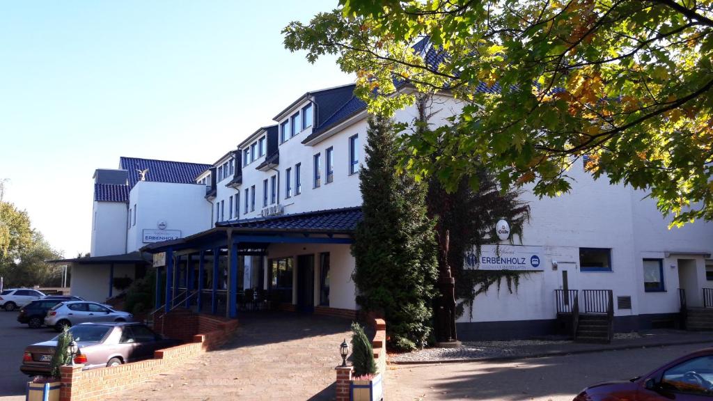 a white building with cars parked in a parking lot at Erbenholz Hotel in Hannover