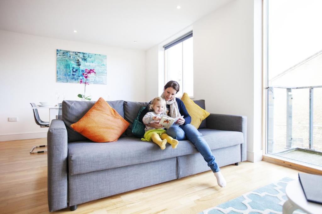 a woman sitting on a couch with a child at Urban's Large 2 bed, 2 bath luxury apartment with secure parking in Oxford