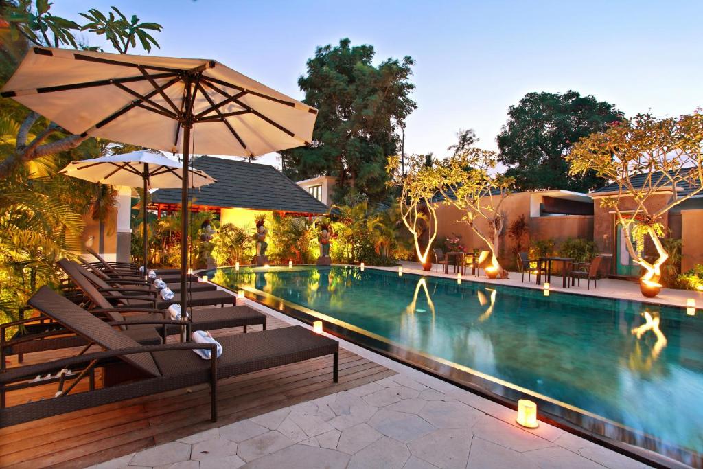 a swimming pool with chairs and an umbrella at New Pondok Sara Villas - CHSE Certified in Seminyak