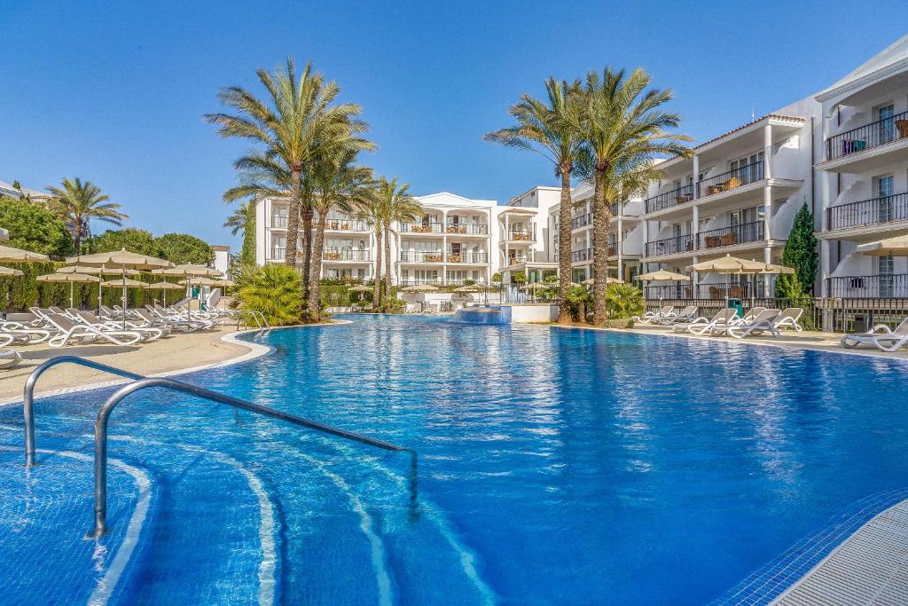 een groot zwembad met palmbomen en gebouwen bij Inturotel Sa Marina in Cala d´Or