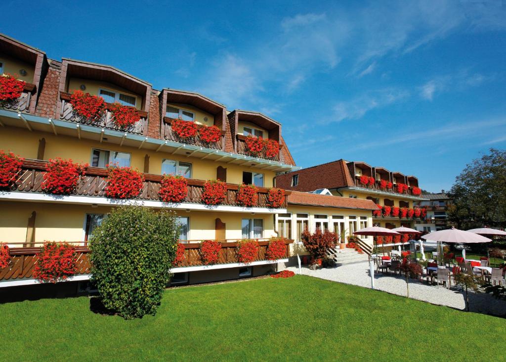 a hotel with flowers on the balconies and a lawn at Hotel Kärnten in Krumpendorf am Wörthersee