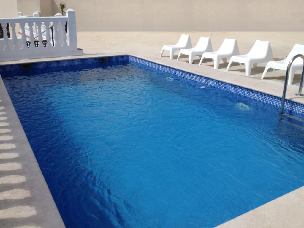 a swimming pool with white chairs and blue water at APARTAMENTOS DOÑA CARMEN - Alojamiento en Málaga capital in Málaga