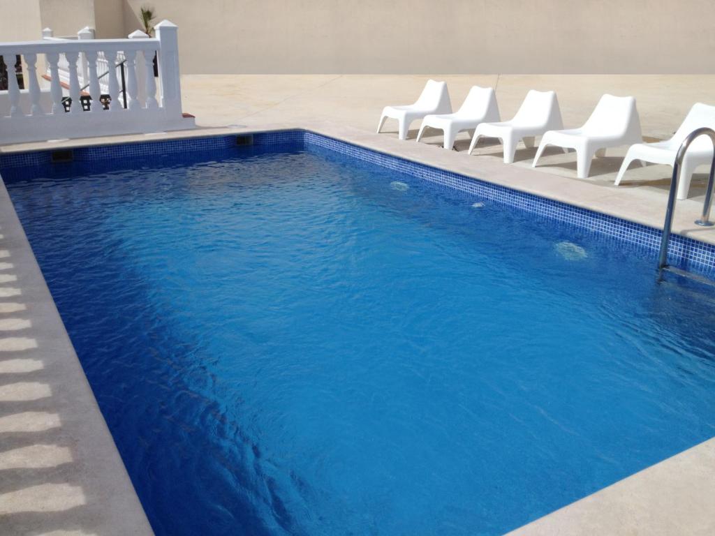a swimming pool with white chairs and blue water at Apartamentos Doña Carmen in Málaga