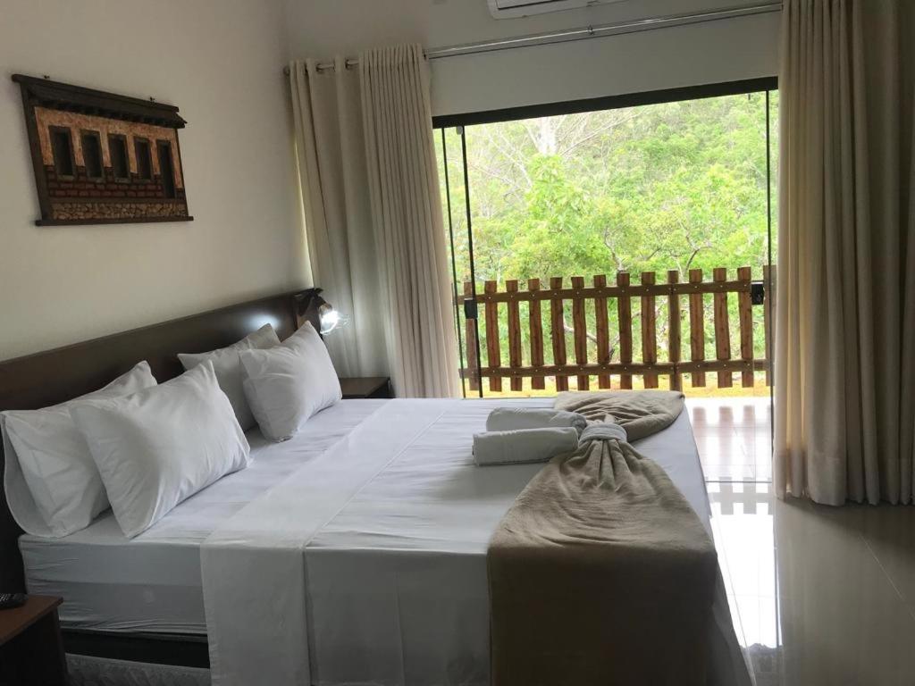 a bedroom with a bed with white sheets and a window at Cachoeira Paraiso in Pirenópolis