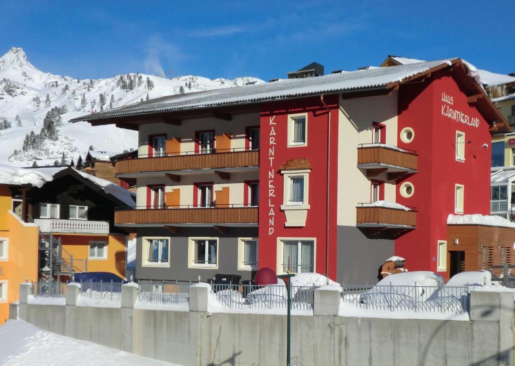 a red hotel with a snow covered mountain in the background at Hotel Kärntnerland in Obertauern