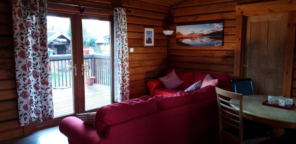 a living room with a red couch and a window at Glenmhor Log Cabin in Fort William