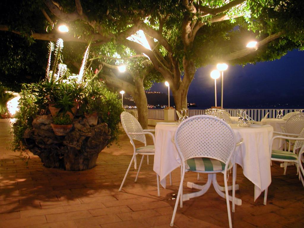 a table with white tables and chairs under a tree at Hotel Lido Mediterranee in Taormina